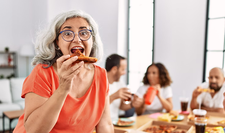 Senior woman enjoying pizza with family, covered by Medigap in Fort Myers